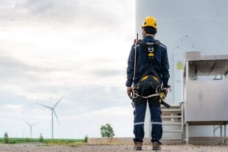 Person looking out across a field of wind turbines. They are in a hard hat and harness