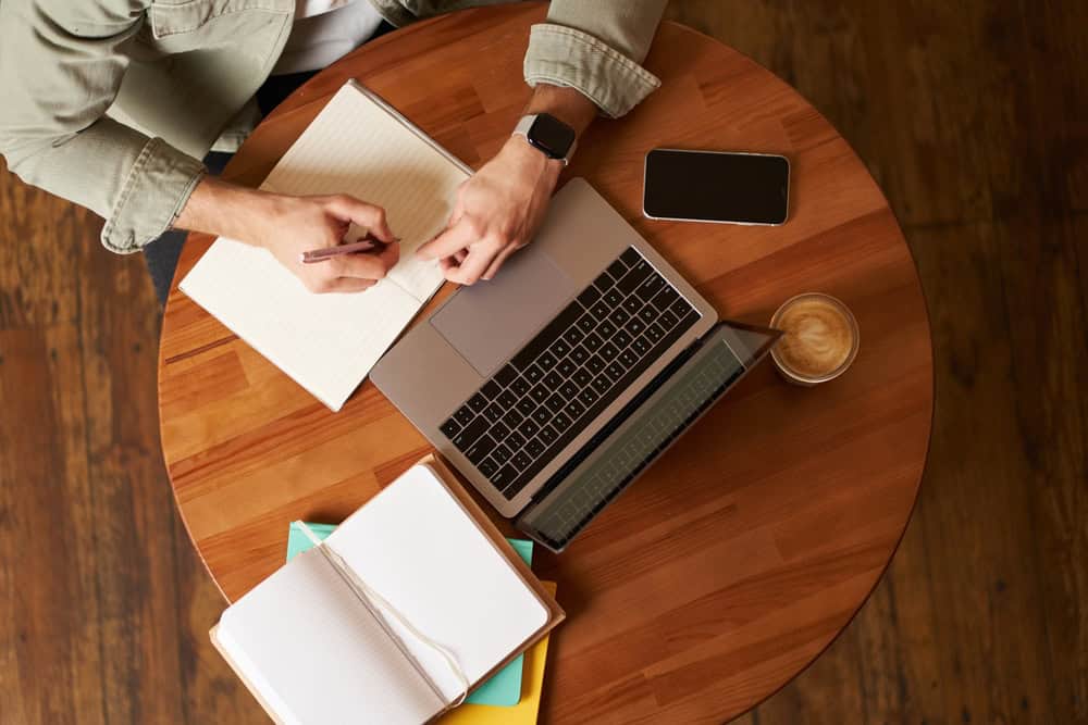 Aerial shot of somebody working on a table with a laptop and note pad