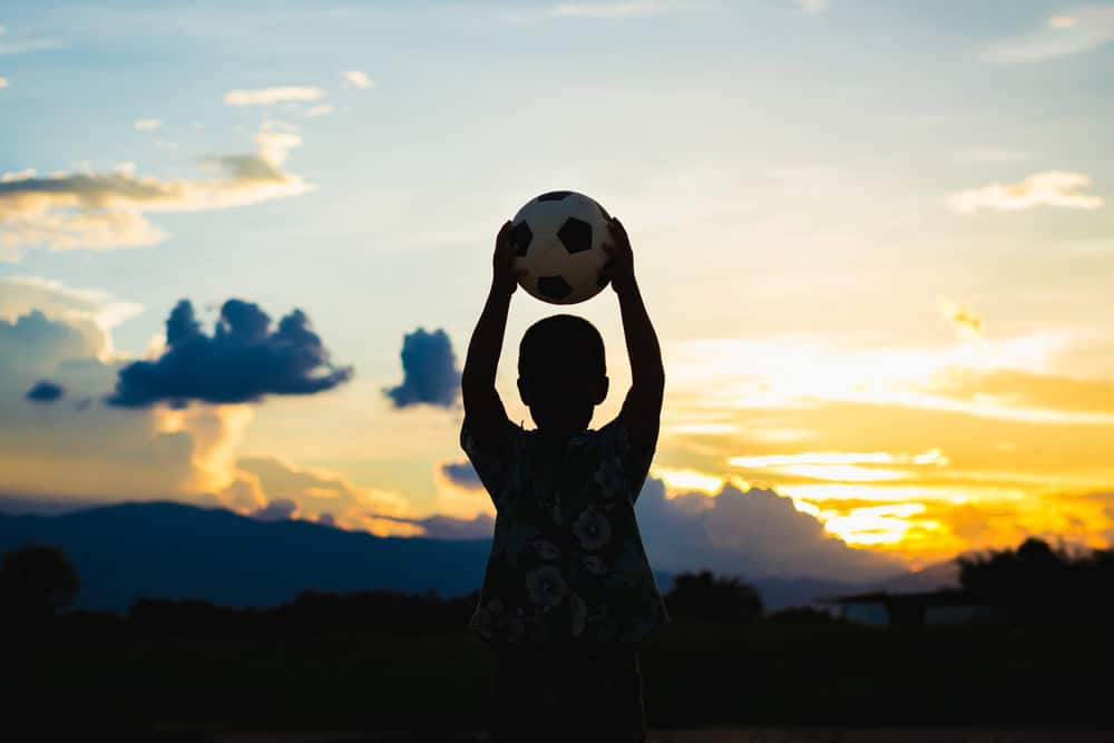 Silhouette of a child holding a football in the air