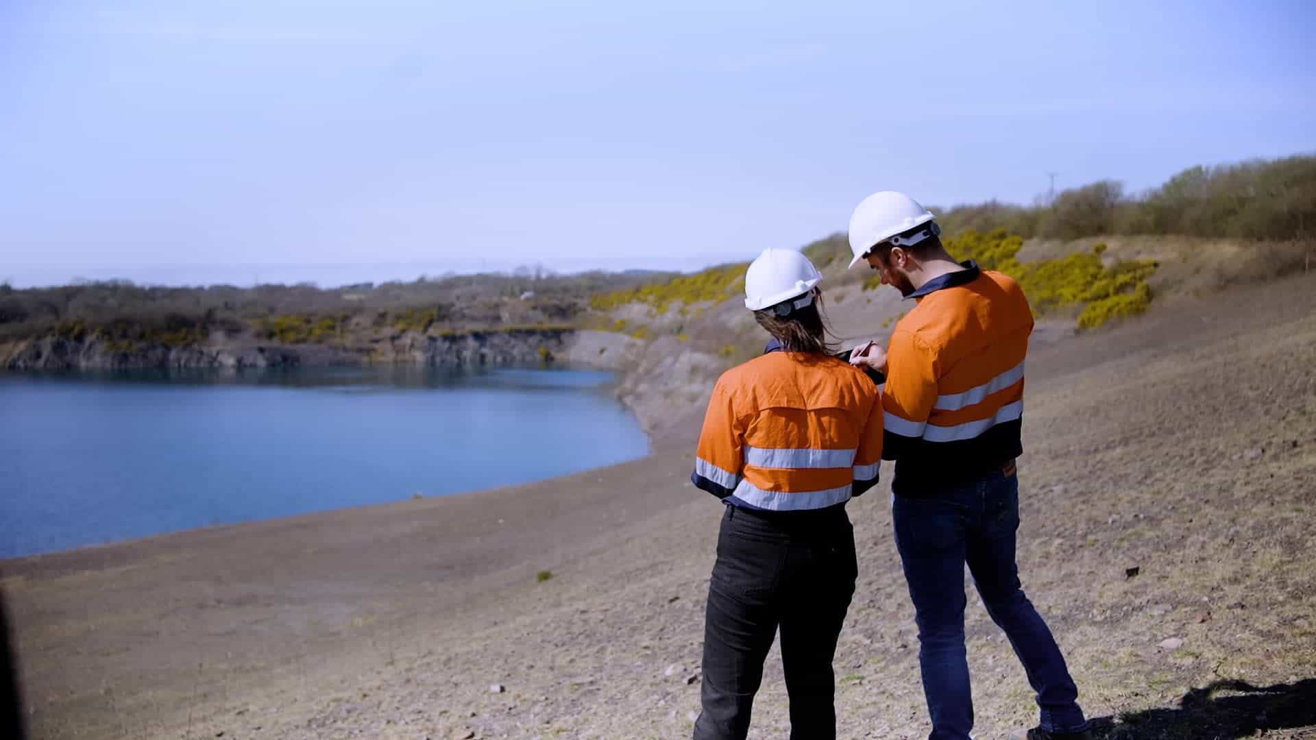Two people in hard hats working on something and overlooking a body of water