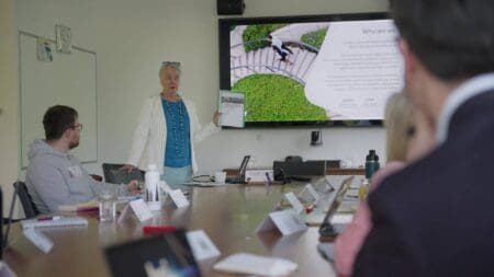 People watching a screen where a woman is stood and talking