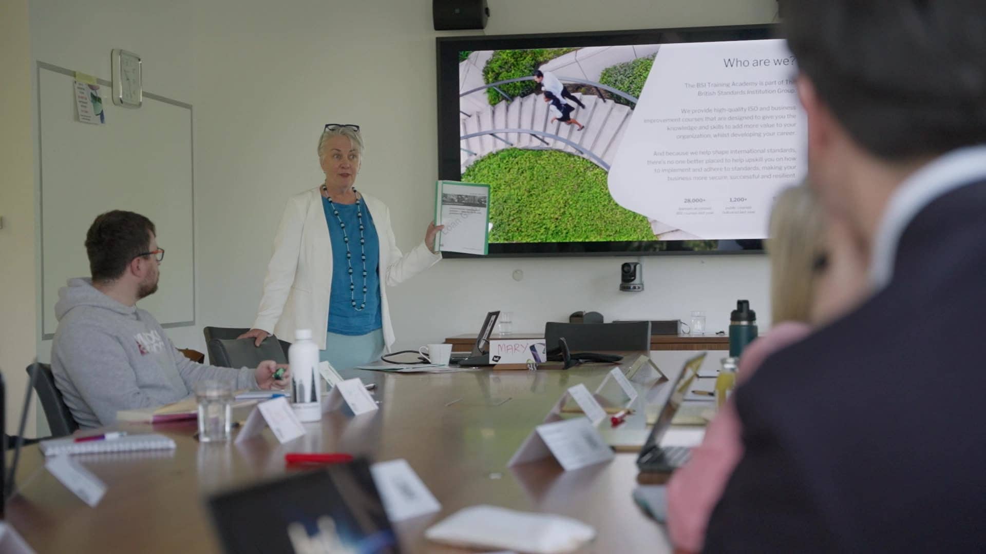 People watching a screen where a woman is stood and talking