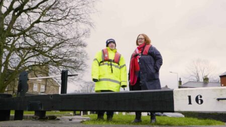 Two people stood by a lock in the UK. one is wearing a high-visibility coat