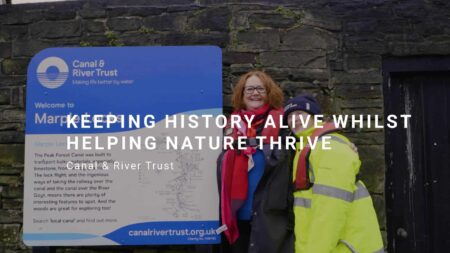 Two people smiling next to a Canal & River Trust sign. title reads: Keeping history alive whilst helping nature thrive
