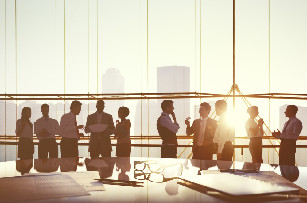 People standing and talking in an office room, with a skyline in the window view in the background