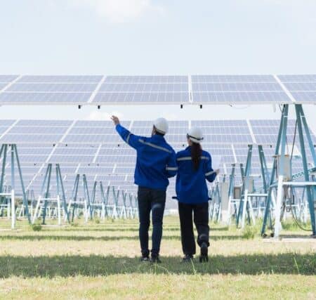 Two people walking through a solar power plant site and pointing at one of the panels