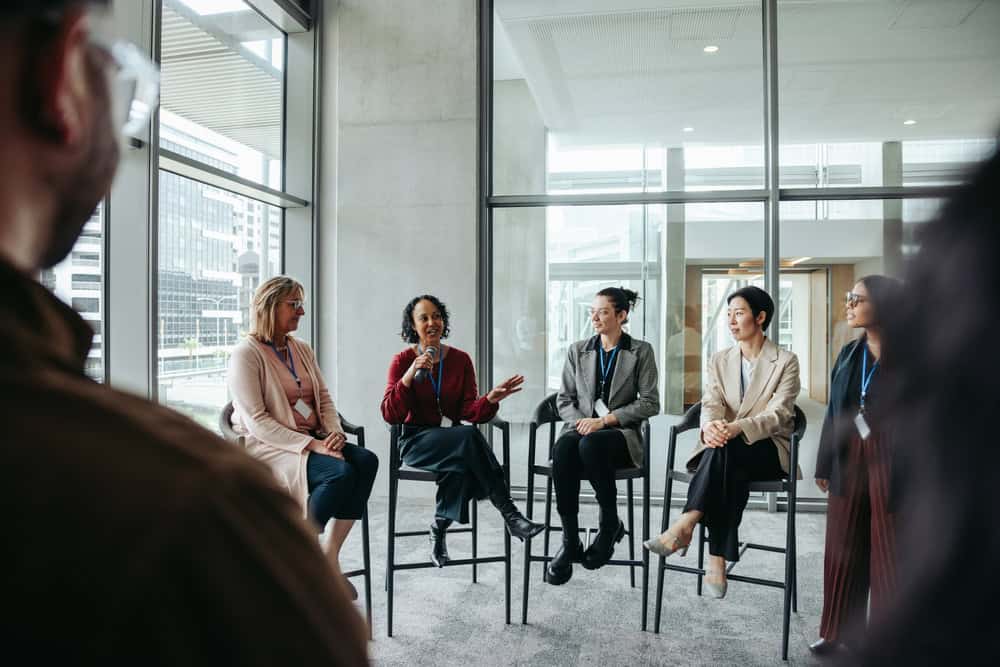 A person doing a speech to a group of people all sat down in a row of chairs