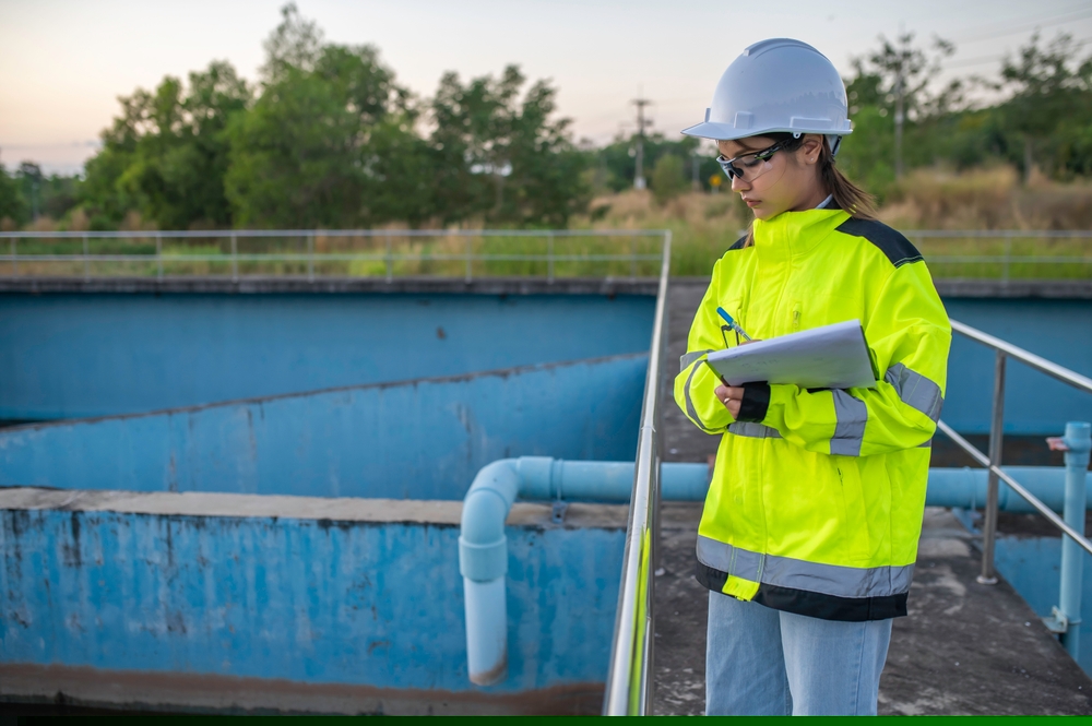 A picture of a woman in a high vis jacket and a hard hat taking notes at a work site