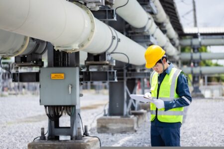 A picture of a man wearing a high vis and a hard hat, taking notes next to machinery