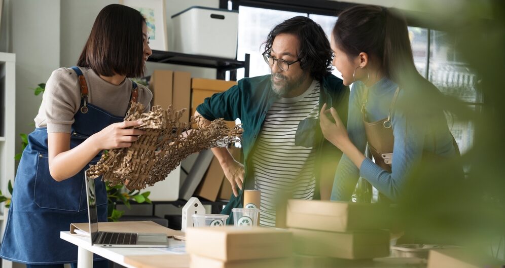 Three people smiling and holding recyclable packaging materials